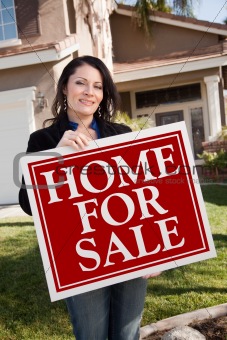 Happy Attractive Hispanic Woman Holding Home For Sale Real Estate Sign In Front of House.