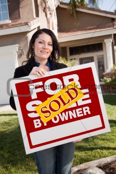 Happy Attractive Hispanic Woman Holding Sold For Sale By Owner Real Estate Sign In Front of House
