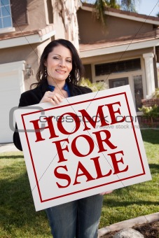Hispanic Woman Holding Home For Sale Real Estate Sign In Front of House.