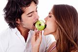 young couple playfully biting green apple