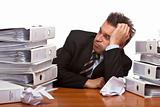 Stressed business man sitting frustrated between folder stacks i