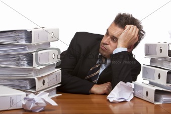 Stressed business man sitting frustrated between folder stacks i