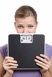 afraid young woman looking behind a weight scale