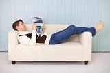 Young woman lies comfortably on sofa with a newspaper
