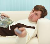 Young man, lying on couch with magazine and TV remote control