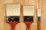 Three Different Sized New Paint Brushes on a Wood Surface.
