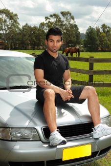 Man sitting on bonnet of silver car in countryside