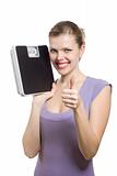 smiling young woman with thumbs up holding a weight scale 