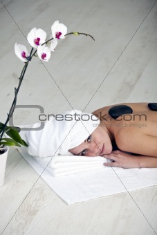 pretty young woman in a spa with stones on her back and a orchid