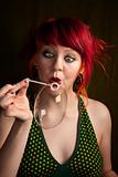 Pretty punky girl with brightly dyed red hair trying to blow a bubble