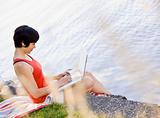 Woman using laptop near pond