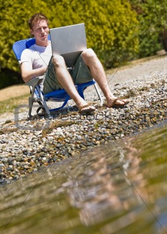Man using laptop near stream