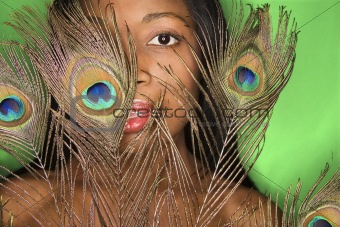 African-American woman looking through peacock feather.