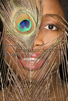 African-American woman looking through peacock feather.