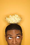 African-American man balancing bowl of popcorn on head.