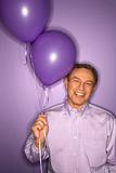 Caucasian man holding purple balloons.
