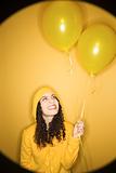 Caucasian woman with balloons wearing yellow raincoat.