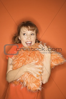 Caucasian woman hugging fuzzy orange pillow.