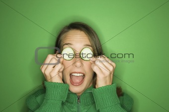 Young Caucasian woman holding cucumber slices over her eyes.