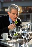 Businessman in suit sitting at outside patio table eating salad.
