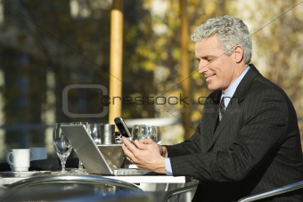Businessman with laptop and dialing cellphone.