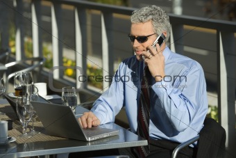 Businessman looking at laptop and talking on cellphone.