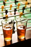 Two glasses of beer at foosball table.