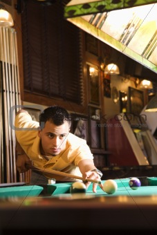 Young man preparing to hit pool ball.