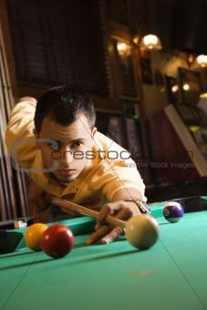 Young man preparing to hit pool ball.