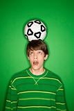 Caucasian teen boy with soccer ball on head. 