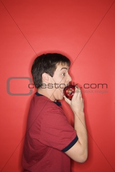 Caucasian teen boy biting apple. 