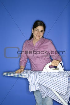 Caucasian teen girl ironing shirt. 