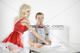 Young man sitting at computer with young  woman pointing.
