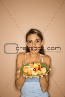 Young woman holding a plate of fruit.