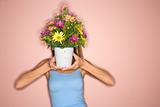 Woman holding pot of flowers in front of her face.