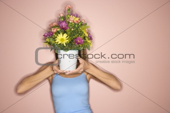 Woman holding pot of flowers in front of her face.