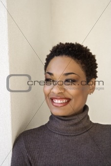 Adult woman leaning against wall smiling.