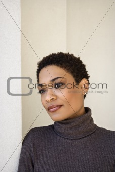 Adult woman leaning against wall looking to side.