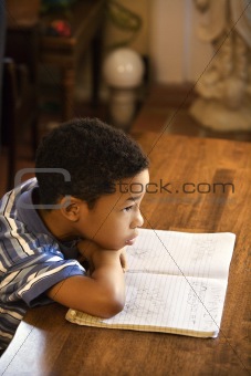 Young boy with head on arms with book in front.