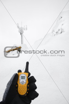 Gloved hand holding walkie talkie in snow scene.