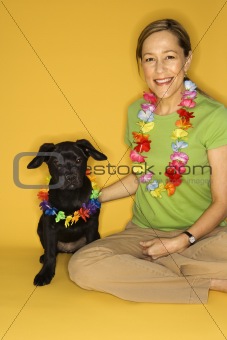 Woman sitting with black puppy wearing leis.