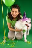 Woman kneeling with  white dog wearing party hat.