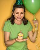 Woman holding cupcake with lit candle.