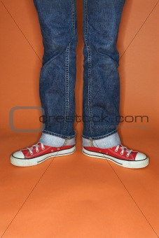 Person in jeans and sneakers with feet turned outward.