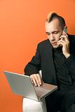 Businessman with mohawk on laptop and cellphone.