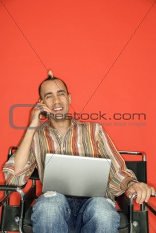 Caucasian man with mohawk using laptop talking on cellphone.