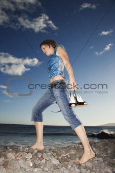 Young adult female walking barefoot on rocky shore.