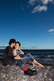 Young adult couple sitting close on beach.