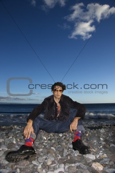 Young adult male sitting on rocky beach.