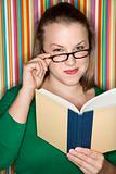 Caucasian female reading and looking at viewer over glasses.